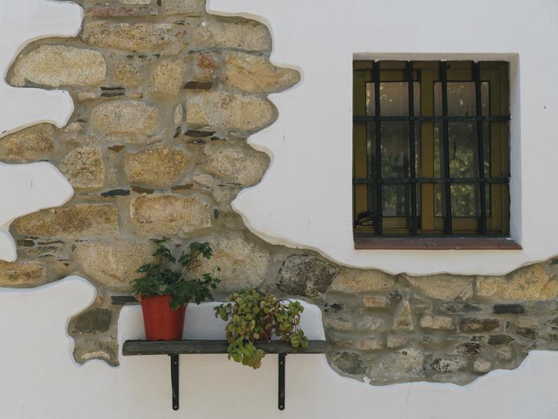 El Ronquillo. Macetas en una fachada de casa blanca con ventana y piedra vista