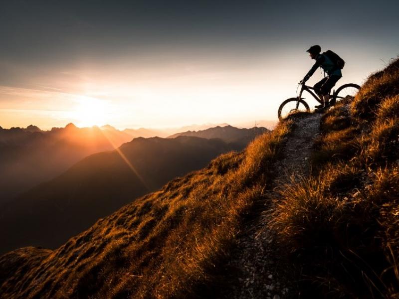 Persona descendiendo en bicicleta un monte a la puesta de sol (contraluz)