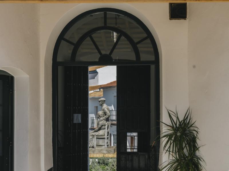 Monumento a los pensionistas visto desde una puerta entreabierta, zócalo de azulejos y una planta
