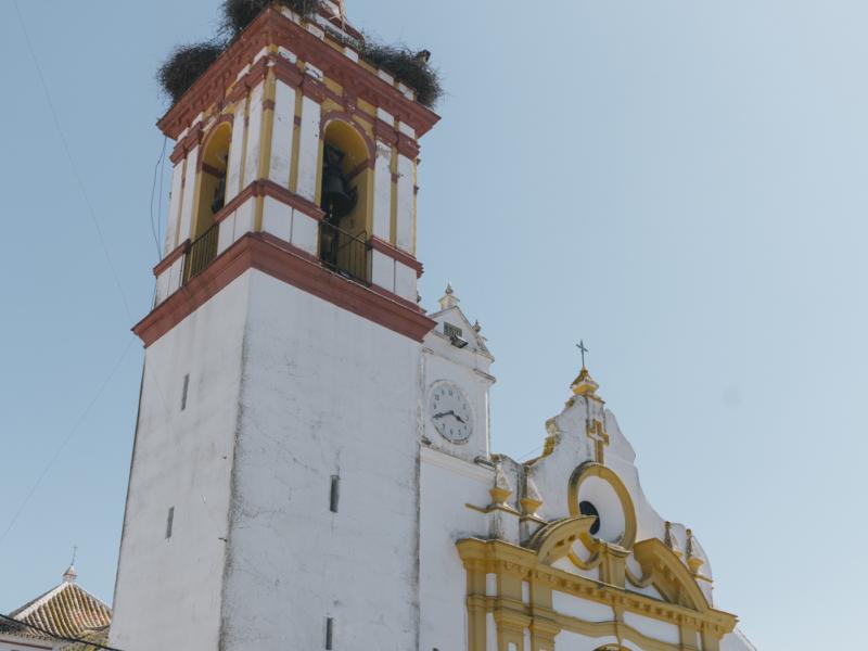 Castilblanco de los Arroyos. Fachada principal de la parroquia, con la torre, nidos de cigüeñas, reloj, azulejos y bancos