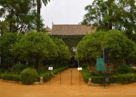 Jardines del palacio de las dueñas, un cartel de audioguia y otro indicando el recorrido, casita con balcón, plantas, árboles y flores